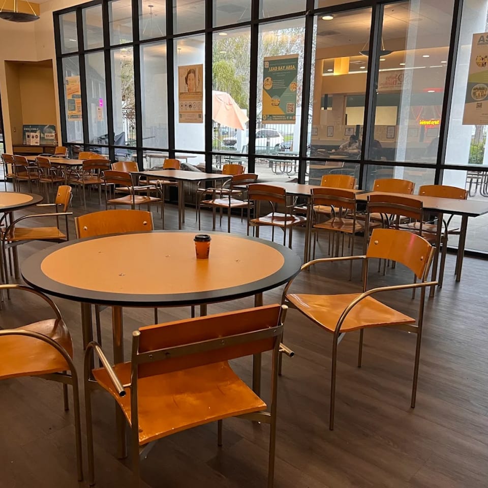 Empty dining area with orange tables and chairs, large windows overlooking an outdoor patio.