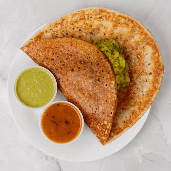 Two golden-brown dosas, one folded, with green chutney, red sambar, and a green potato filling.