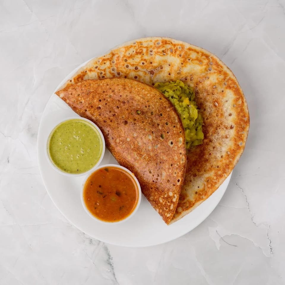 Two golden-brown dosas with green chutney and orange sambar on a white plate.
