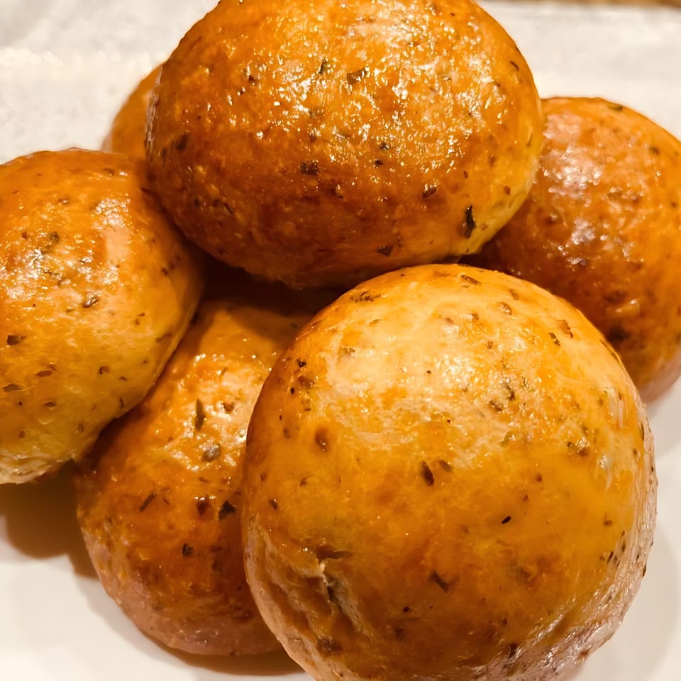 Close-up of several golden-brown, glazed bread rolls with herbs on a white plate.